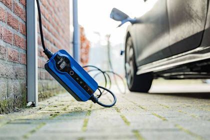 Blue Voldt mobile EV charging cable with control box on a brick wall while charging a car