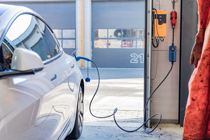 White Tesla charging in front of a garage with a blue Voldt EV charging cable