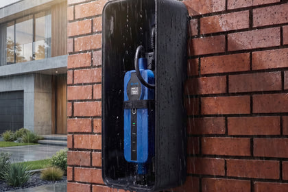 Blue portable charger inside a wall box on a brick facade during rainfall