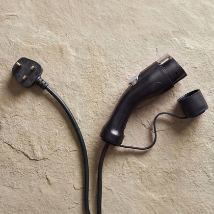 Type 1 connector and UK plug of the Voldt® Portable Charger on a beige stone surface